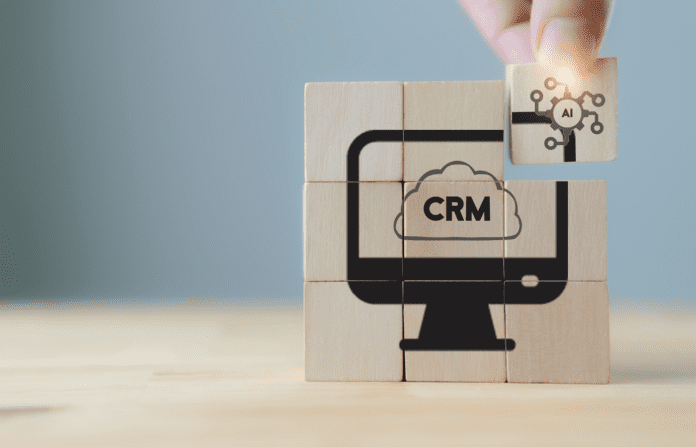 Hand holding wooden cube puzzle with AI-CRM icon on grey background.